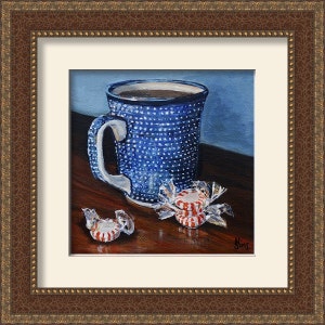 Puede incluir: Una taza de cer&aacute;mica azul y blanca con asa marr&oacute;n llena de caf&eacute;, sentada sobre una mesa de madera con tres caramelos de menta roja y blanca sin envolver.