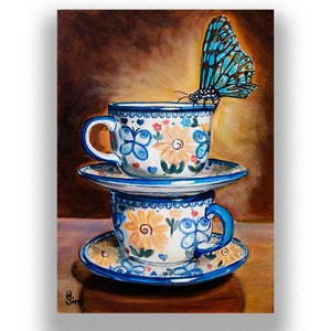 May include: Two blue and white teacups with floral patterns are stacked on top of each other. The top cup has a blue butterfly perched on the rim. The cups are on a wooden surface.