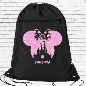 May include: Black drawstring backpack featuring a pink glitter Minnie Mouse silhouette with a polka dot bow and a castle design. The name "LORENNA" is printed below the castle. The bag has a zippered pocket and black drawstrings.
