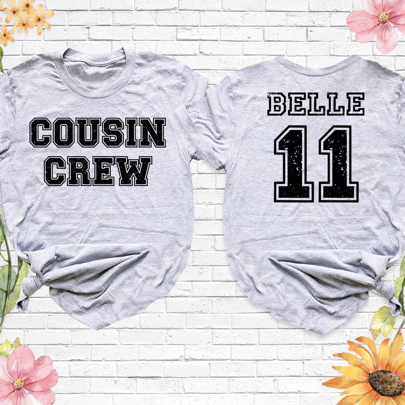 Op de afbeelding: Twee lichtgrijze t-shirts. E&eacute;n shirt heeft de woorden "COUSIN CREW" in een zwarte, blokletter. Het andere shirt heeft het woord "BELLE" boven het nummer "11" in een zwarte, blokletter. De shirts staan op een witte bakstenen achtergrond.
