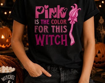 May include: A black short-sleeved t-shirt featuring the pink text "Pink is the color for this witch" with heart accents and a graphic of a stylized pink witch's broomstick with a bow. The design is centered on the front of the shirt.