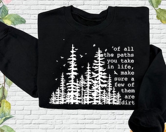 May include: A black crewneck sweatshirt featuring a white graphic of a forest of pine trees and birds. The text reads: Of all the paths you take in life, make sure a few of them are dirt. The design is centered on the front of the garment.