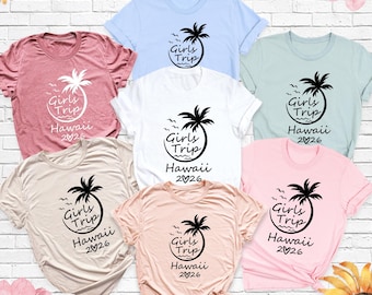 May include: A collection of six short-sleeved crew neck t-shirts in various pastel colors, each featuring a black graphic of a palm tree with the text Girls Trip, Hawaii, and 2026 with a heart symbol replacing the zero.