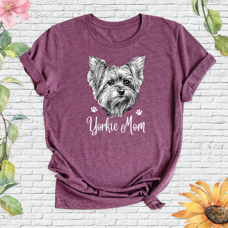 May include: A purple t-shirt with a black and white illustration of a Yorkshire Terrier and the text "Yorkie Mom" in white.