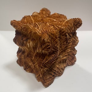 May include: A brown ceramic sculpture with a textured surface. The sculpture is shaped like a cube with rounded edges.