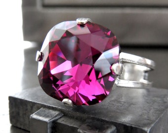 May include: A silver ring with a large, faceted, cushion-cut, magenta gemstone.