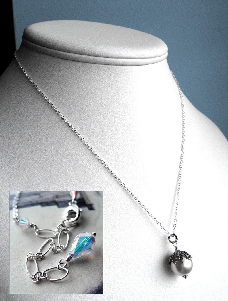May include: A silver chain necklace with a pearl pendant. The pendant has a silver crown design and a white pearl.