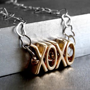 May include: A gold necklace with a chain made of silver metal. The pendant is made of gold and spells out "XOXO".