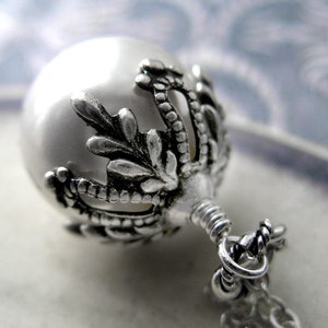 May include: A silver pendant with a white pearl and a detailed floral design. The pendant is attached to a silver chain.