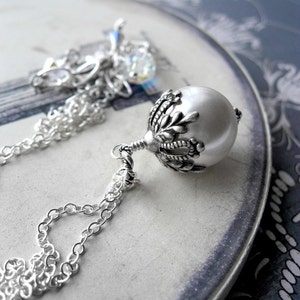 May include: A silver chain necklace with a pearl pendant. The pendant has a detailed silver design with a floral motif.