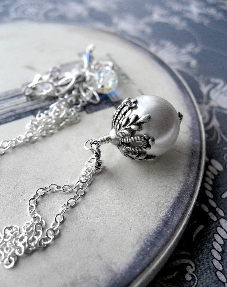 May include: A silver chain necklace with a pearl pendant. The pendant has a detailed silver design with a floral motif.