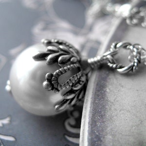 May include: A silver necklace with a large pearl pendant. The pendant is surrounded by a detailed silver design.