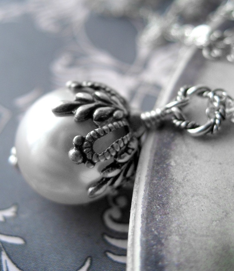 May include: A silver necklace with a large pearl pendant. The pendant is surrounded by a detailed silver design.