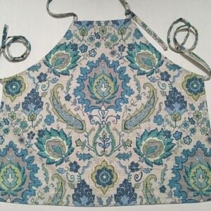 May include: A blue and green patterned apron with adjustable straps. The apron has a paisley design with a white background.