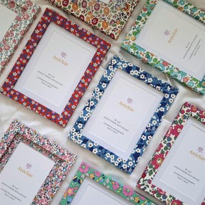 Può includere: Una collezione di cornici per foto con motivi floreali in vari colori, tra cui rosso, blu e rosa. Ogni cornice ha un passe-partout bianco e il testo "Anichie". Adatte per foto di 15 x 10 cm.