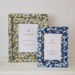 May include: Two floral photo frames. One is green with white flowers, the other is blue with white flowers. The frames have white inserts with the brand name "Anichie" and text indicating the frame sizes are 7"x5" and 6"x4".