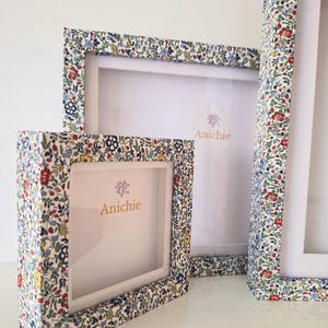 May include: A set of three picture frames with floral fabric covering the borders. The frames are white inside with the brand name "Anichie" printed in gold. The floral pattern includes red, blue, and yellow flowers on a white background.