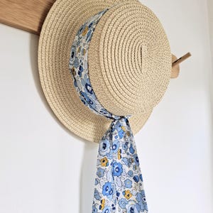 May include: A straw hat with a wide brim and a blue and white floral ribbon tied around the crown. The ribbon is tied in a bow at the back of the hat.