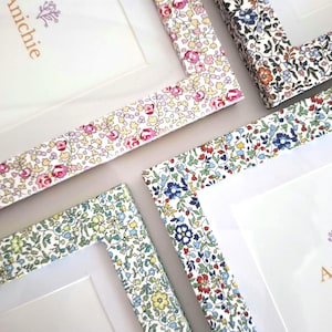 May include: Three rectangular photo frames featuring a colourful floral pattern on the borders. Each frame includes a white mount and a paper insert with the text Anichie and the dimensions 6 inches by 4 inches printed in orange and purple.