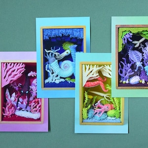 以下が含まれることがあります： 水中のシーンを描いた4つの額装されたアート作品。各フレームには、サンゴ、タコ、その他の海の生き物など、海洋生物の詳細なジオラマが含まれています。フレームは緑色の背景に配置され、各フレームには異なる色のボーダーがあります。