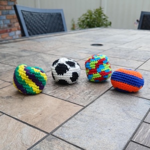 May include: Four crocheted balls in different colours and patterns. The balls are on a tiled surface. The balls are green and yellow, black and white, red and blue, and orange and blue.
