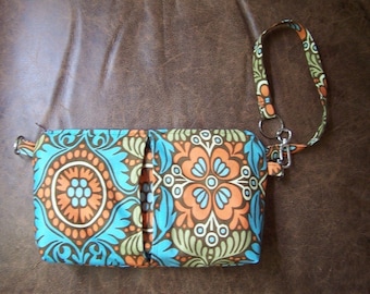 Pode incluir: Uma pequena bolsa de tecido com padrão azul, laranja e verde, com uma alça marrom e um chaveiro prateado.