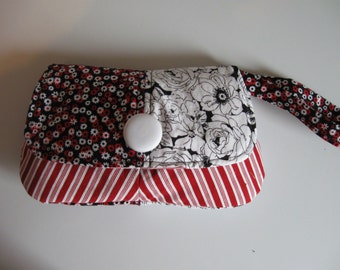 Pode incluir: Uma pequena bolsa de tecido floral preto e branco com um fundo de tecido listrado vermelho e branco e um fecho de botão branco. A bolsa tem uma alça de tecido floral preto e branco.