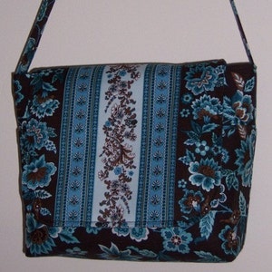 Puede incluir: Un bolso bandolera de tela con estampado azul y marrón con una correa larga ajustable.