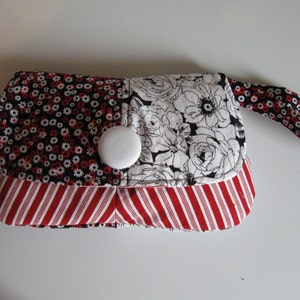 May include: A small black and white floral fabric purse with a red and white striped fabric bottom and a white button closure. The purse has a black and white floral fabric strap.