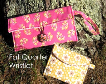 Puede incluir: Dos bolsas de tela, una rosa con un estampado floral y una correa para la muñeca, y otra amarilla con un estampado floral blanco. La bolsa rosa está etiquetada como "Fat Quarter Wristlet" y la bolsa amarilla está etiquetada como "Key Chain Wallet".