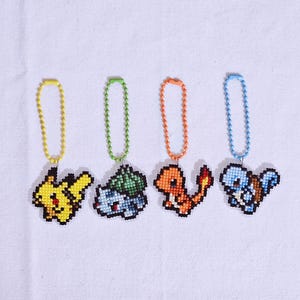 May include: Four pixelated character keychains: Pikachu, Bulbasaur, Charmander, and Squirtle. Each keychain features a different character design with a colorful chain. The keychains are made with a cross-stitch technique.