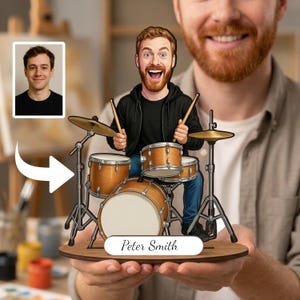 Op de afbeelding: Een gepersonaliseerd houten beeldje van een drummer in cartoonstijl met een rode baard, gekleed in een zwarte hoodie en blauwe jeans, zittend achter een lichtbruin drumstel met zilverkleurige hardware. Een wit naamplaatje onderaan toont de tekst Peter Smith.