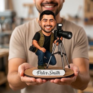 May include: A custom wooden cutout figure of a photographer with a beard, wearing a black t-shirt, olive vest, and blue jeans, kneeling beside a camera on a tripod. The figure is mounted on a round wooden base with the name Peter Smith printed.