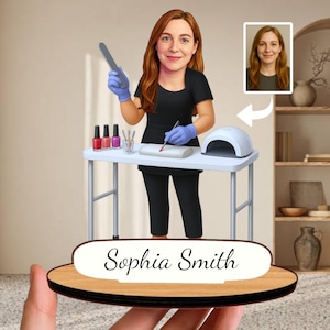 Può includere: Statuetta in legno personalizzata di un'onicotecnica, Sophia Smith, al lavoro. La figura indossa un'uniforme nera e guanti blu, con una lima per unghie e un pennello. Flaconi di smalto e una lampada UV sono sul tavolo. Una foto della persona è sullo sfondo.