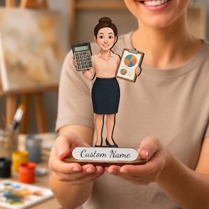 Può includere: Una statuetta in legno di una persona professionale con capelli castani raccolti in uno chignon, che indossa una camicia rosa chiaro e una gonna blu scuro. La figura tiene una calcolatrice grigia e una cartellina con un grafico a torta.