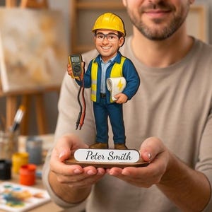 Könnte beinhalten: Eine individuelle Elektriker-Figur mit gelbem Schutzhelm, blauem Hemd, blauer Hose und gelber Warnweste. Die Figur hält ein digitales Multimeter und eine weiße Papierrolle mit gelbem Blitzsymbol und steht auf einem Sockel mit der Aufschrift Peter Smith.