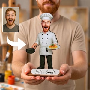 Può includere: Una statuetta bobblehead personalizzata di uno chef con la barba rossa, che indossa un cappello e una giacca da chef bianchi con pantaloni scuri. La figura tiene in mano una padella nera e un piatto di spaghetti, su una base con il nome Peter Smith.