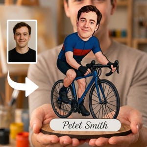 May include: A custom caricature figurine of a cyclist riding a blue road bike, mounted on a circular wooden base with a white plaque displaying the name Petet Smith. The figure wears a blue and red jersey, black shorts, and black cycling shoes.