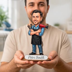 Peut inclure: Une figurine en bois découpée représentant un coiffeur barbu portant une chemise bleue et un tablier noir, tenant un peigne et un sèche-cheveux rouge. La figurine repose sur un socle avec le nom Peter Smith écrit en noir sur une étiquette blanche.