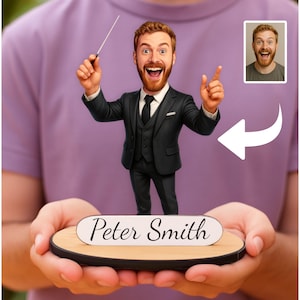 Könnte beinhalten: Figur eines Mannes in einem schwarzen Anzug, der einen Dirigentenstab hält, mit dem Namen "Peter Smith" auf dem Sockel. Die Figur hat ein cartoonartiges Design mit einem lächelnden Gesicht und einem kleinen Bild des Gesichts des Mannes.