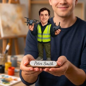 Peut inclure: Une figurine personnalisée à tête branlante représentant une personne portant un sweat à capuche sombre, un gilet jaune haute visibilité et un pantalon cargo vert olive. La figurine tient un petit drone gris et une télécommande noire, fixée sur un socle en bois avec le nom Peter Smith inscrit sur une plaque blanche.
