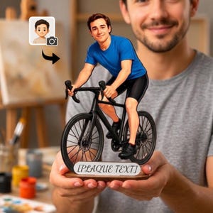 Könnte beinhalten: Eine individuelle Figur einer Person mit braunen Haaren, die ein blaues T-Shirt und eine schwarze Shorts trägt und auf einem schwarzen Fahrrad sitzt. Die Figur steht auf einem Holzsockel mit einem weißen Schild mit der Aufschrift PLAQUE TEXT.