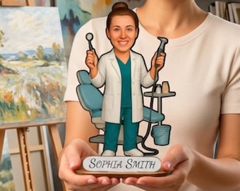 May include: A custom acrylic cutout featuring a cartoon dentist in a white lab coat and teal scrubs, holding dental tools. The figure stands in front of a blue dental chair and a small table, with a base plate displaying the name Sophia Smith.