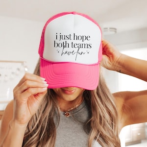 Peut inclure: Casquette de camionneur rose et blanche avec le texte "i just hope both teams have fun" en noir.