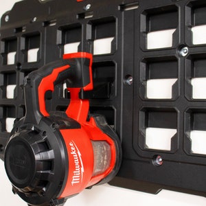 May include: A red and black Milwaukee power blower tool hanging on a black pegboard wall.