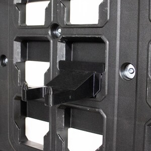 May include: A black plastic wall-mounted storage system with a black plastic hook attached to it.