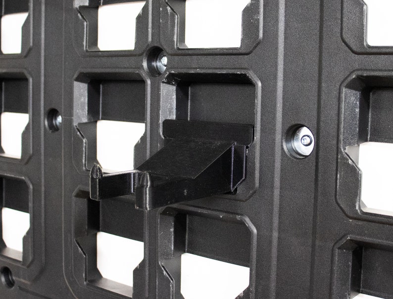 May include: A black plastic wall-mounted storage system with a black plastic hook attached to it.