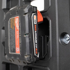 May include: A black Milwaukee M18 REDLITHIUM CP2.0 battery pack, 16V 36Wh, is inserted into a black mounting bracket. The battery pack has red and white labels with product information. The bracket has a textured surface.