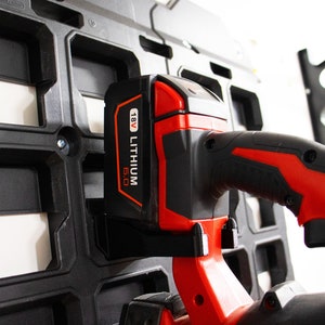 May include: A red and black power tool with a 18V Lithium 6.0 battery attached. The tool is hanging on a black plastic wall mount.