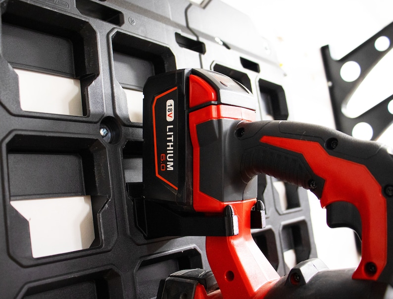May include: A red and black power tool with a 18V Lithium 6.0 battery attached. The tool is hanging on a black plastic wall mount.